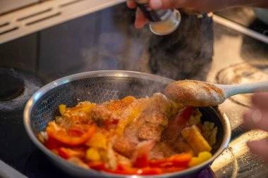 Yakın çekim, yüksek detay makro çekim. Bir kadın tavuk sotesi hazırlarken, cızırtılı malzemeler sergilerken ve sıcak bir mutfak ortamında yemek pişirirken görülüyor.