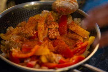 Yakın çekim, yüksek detay makro çekim. Bir kadın tavuk sotesi hazırlarken, cızırtılı malzemeler sergilerken ve sıcak bir mutfak ortamında yemek pişirirken görülüyor.