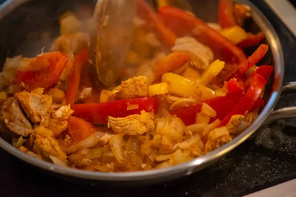 Yakın çekim, yüksek detay makro çekim. Bir kadın tavuk sotesi hazırlarken, cızırtılı malzemeler sergilerken ve sıcak bir mutfak ortamında yemek pişirirken görülüyor.