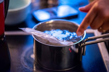 Yakın çekim, yüksek detay makro çekim. Bir kadın tavuk sotesi hazırlarken, cızırtılı malzemeler sergilerken ve sıcak bir mutfak ortamında yemek pişirirken görülüyor.