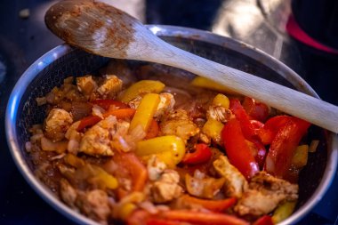 Yakın çekim, yüksek detay makro çekim. Bir kadın tavuk sotesi hazırlarken, cızırtılı malzemeler sergilerken ve sıcak bir mutfak ortamında yemek pişirirken görülüyor.