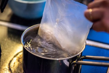 Yakın çekim, yüksek detay makro çekim. Bir kadın tavuk sotesi hazırlarken, cızırtılı malzemeler sergilerken ve sıcak bir mutfak ortamında yemek pişirirken görülüyor.