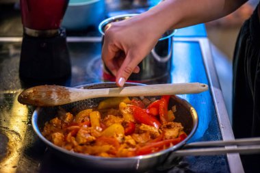 Yakın çekim, yüksek detay makro çekim. Bir kadın tavuk sotesi hazırlarken, cızırtılı malzemeler sergilerken ve sıcak bir mutfak ortamında yemek pişirirken görülüyor.