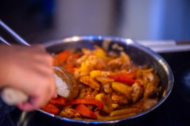 Yakın çekim, yüksek detay makro çekim. Bir kadın tavuk sotesi hazırlarken, cızırtılı malzemeler sergilerken ve sıcak bir mutfak ortamında yemek pişirirken görülüyor.