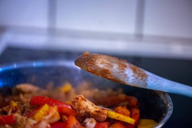 Yakın çekim, yüksek detay makro çekim. Bir kadın tavuk sotesi hazırlarken, cızırtılı malzemeler sergilerken ve sıcak bir mutfak ortamında yemek pişirirken görülüyor.