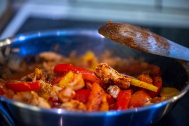 Yakın çekim, yüksek detay makro çekim. Bir kadın tavuk sotesi hazırlarken, cızırtılı malzemeler sergilerken ve sıcak bir mutfak ortamında yemek pişirirken görülüyor.