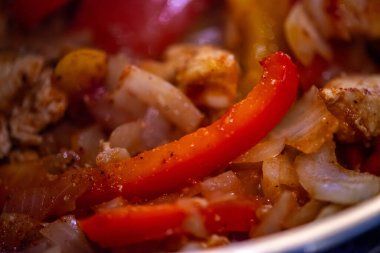 Yakın çekim, yüksek detay makro çekim. Bir kadın tavuk sotesi hazırlarken, cızırtılı malzemeler sergilerken ve sıcak bir mutfak ortamında yemek pişirirken görülüyor.