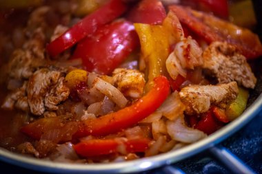 Yakın çekim, yüksek detay makro çekim. Bir kadın tavuk sotesi hazırlarken, cızırtılı malzemeler sergilerken ve sıcak bir mutfak ortamında yemek pişirirken görülüyor.