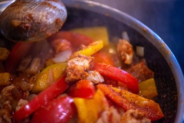 Yakın çekim, yüksek detay makro çekim. Bir kadın tavuk sotesi hazırlarken, cızırtılı malzemeler sergilerken ve sıcak bir mutfak ortamında yemek pişirirken görülüyor.