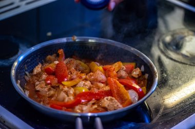 Yakın çekim, yüksek detay makro çekim. Bir kadın tavuk sotesi hazırlarken, cızırtılı malzemeler sergilerken ve sıcak bir mutfak ortamında yemek pişirirken görülüyor.