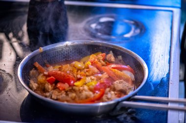 Yakın çekim, yüksek detay makro çekim. Bir kadın tavuk sotesi hazırlarken, cızırtılı malzemeler sergilerken ve sıcak bir mutfak ortamında yemek pişirirken görülüyor.