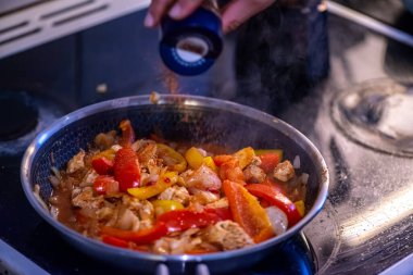 Yakın çekim, yüksek detay makro çekim. Bir kadın tavuk sotesi hazırlarken, cızırtılı malzemeler sergilerken ve sıcak bir mutfak ortamında yemek pişirirken görülüyor.