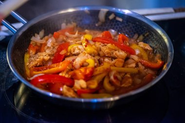 Yakın çekim, yüksek detay makro çekim. Bir kadın tavuk sotesi hazırlarken, cızırtılı malzemeler sergilerken ve sıcak bir mutfak ortamında yemek pişirirken görülüyor.