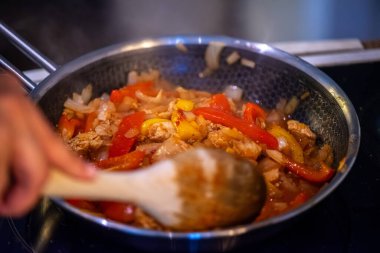 Yakın çekim, yüksek detay makro çekim. Bir kadın tavuk sotesi hazırlarken, cızırtılı malzemeler sergilerken ve sıcak bir mutfak ortamında yemek pişirirken görülüyor.