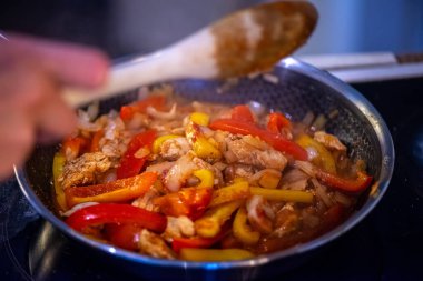 Yakın çekim, yüksek detay makro çekim. Bir kadın tavuk sotesi hazırlarken, cızırtılı malzemeler sergilerken ve sıcak bir mutfak ortamında yemek pişirirken görülüyor.