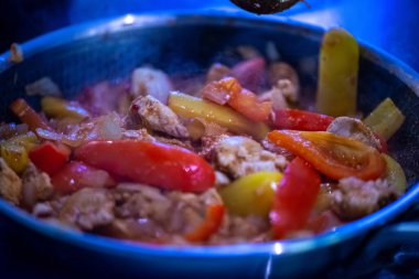 Yakın çekim, yüksek detay makro çekim. Bir kadın tavuk sotesi hazırlarken, cızırtılı malzemeler sergilerken ve sıcak bir mutfak ortamında yemek pişirirken görülüyor.