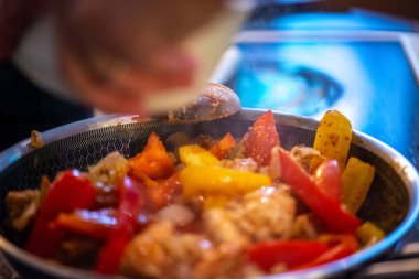 Yakın çekim, yüksek detay makro çekim. Bir kadın tavuk sotesi hazırlarken, cızırtılı malzemeler sergilerken ve sıcak bir mutfak ortamında yemek pişirirken görülüyor.