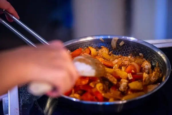 Yakın çekim, yüksek detay makro çekim. Bir kadın tavuk sotesi hazırlarken, cızırtılı malzemeler sergilerken ve sıcak bir mutfak ortamında yemek pişirirken görülüyor.