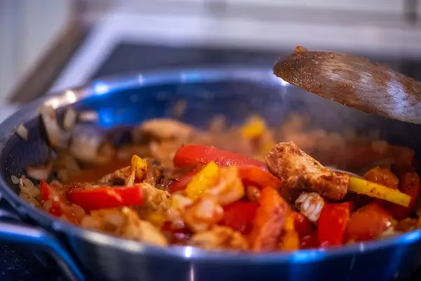 Yakın çekim, yüksek detay makro çekim. Bir kadın tavuk sotesi hazırlarken, cızırtılı malzemeler sergilerken ve sıcak bir mutfak ortamında yemek pişirirken görülüyor.