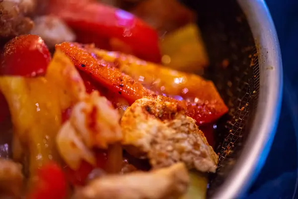 Yakın çekim, yüksek detay makro çekim. Bir kadın tavuk sotesi hazırlarken, cızırtılı malzemeler sergilerken ve sıcak bir mutfak ortamında yemek pişirirken görülüyor.