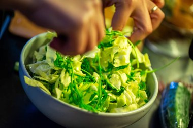 Salatalık, marul ve diğer sebzeleri dilimleyen bir kadının ev yapımı salatanın tazeliğini ve sağlığını yakaladığı canlı bir mutfak sahnesi..