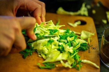 Salatalık, marul ve diğer sebzeleri dilimleyen bir kadının ev yapımı salatanın tazeliğini ve sağlığını yakaladığı canlı bir mutfak sahnesi..