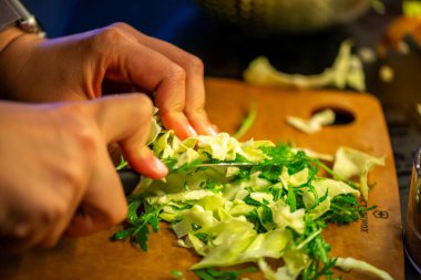 Salatalık, marul ve diğer sebzeleri dilimleyen bir kadının ev yapımı salatanın tazeliğini ve sağlığını yakaladığı canlı bir mutfak sahnesi..
