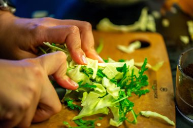Salatalık, marul ve diğer sebzeleri dilimleyen bir kadının ev yapımı salatanın tazeliğini ve sağlığını yakaladığı canlı bir mutfak sahnesi..