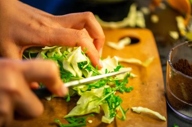 Salatalık, marul ve diğer sebzeleri dilimleyen bir kadının ev yapımı salatanın tazeliğini ve sağlığını yakaladığı canlı bir mutfak sahnesi..