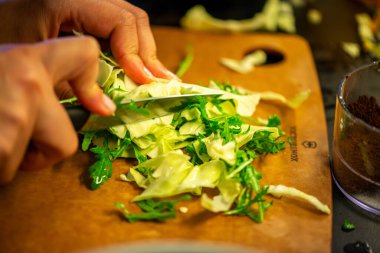 Salatalık, marul ve diğer sebzeleri dilimleyen bir kadının ev yapımı salatanın tazeliğini ve sağlığını yakaladığı canlı bir mutfak sahnesi..