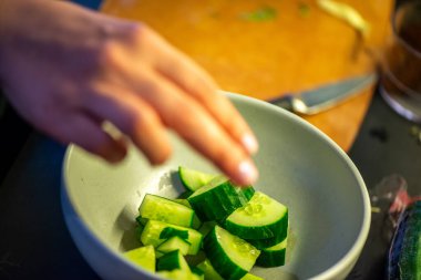 Salatalık, marul ve diğer sebzeleri dilimleyen bir kadının ev yapımı salatanın tazeliğini ve sağlığını yakaladığı canlı bir mutfak sahnesi..