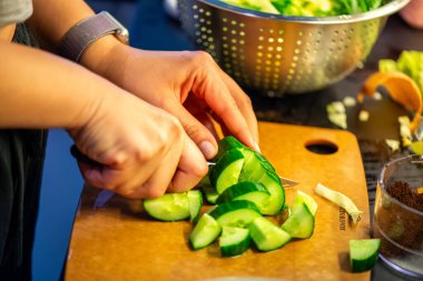 Salatalık, marul ve diğer sebzeleri dilimleyen bir kadının ev yapımı salatanın tazeliğini ve sağlığını yakaladığı canlı bir mutfak sahnesi..