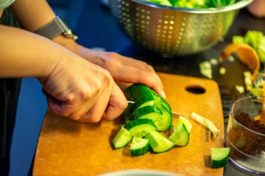 Salatalık, marul ve diğer sebzeleri dilimleyen bir kadının ev yapımı salatanın tazeliğini ve sağlığını yakaladığı canlı bir mutfak sahnesi..