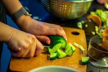 Salatalık, marul ve diğer sebzeleri dilimleyen bir kadının ev yapımı salatanın tazeliğini ve sağlığını yakaladığı canlı bir mutfak sahnesi..