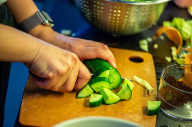Salatalık, marul ve diğer sebzeleri dilimleyen bir kadının ev yapımı salatanın tazeliğini ve sağlığını yakaladığı canlı bir mutfak sahnesi..