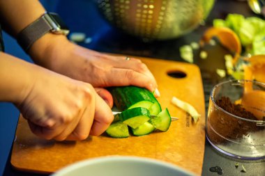 Salatalık, marul ve diğer sebzeleri dilimleyen bir kadının ev yapımı salatanın tazeliğini ve sağlığını yakaladığı canlı bir mutfak sahnesi..