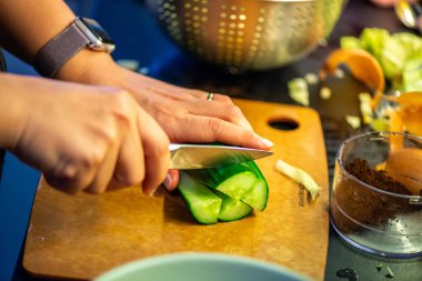 Salatalık, marul ve diğer sebzeleri dilimleyen bir kadının ev yapımı salatanın tazeliğini ve sağlığını yakaladığı canlı bir mutfak sahnesi..