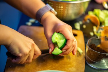 Salatalık, marul ve diğer sebzeleri dilimleyen bir kadının ev yapımı salatanın tazeliğini ve sağlığını yakaladığı canlı bir mutfak sahnesi..
