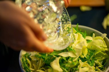 Canlı bir makro fotoğraf taze bir limonu dilimleyen ve meyve suyunu renkli bir salatanın üzerine sıkan bir kadını yakalıyor, narenciye dokusunu ve mutfak faaliyetlerindeki tazeliği vurguluyor..