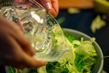 Canlı bir makro fotoğraf taze bir limonu dilimleyen ve meyve suyunu renkli bir salatanın üzerine sıkan bir kadını yakalıyor, narenciye dokusunu ve mutfak faaliyetlerindeki tazeliği vurguluyor..
