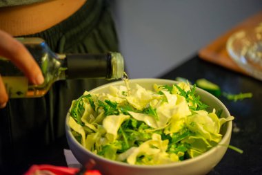 Canlı bir makro fotoğraf taze bir limonu dilimleyen ve meyve suyunu renkli bir salatanın üzerine sıkan bir kadını yakalıyor, narenciye dokusunu ve mutfak faaliyetlerindeki tazeliği vurguluyor..