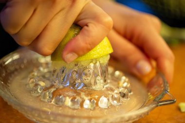 Canlı bir makro fotoğraf taze bir limonu dilimleyen ve meyve suyunu renkli bir salatanın üzerine sıkan bir kadını yakalıyor, narenciye dokusunu ve mutfak faaliyetlerindeki tazeliği vurguluyor..