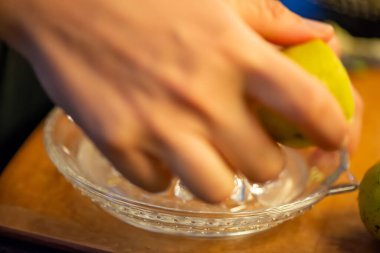 Canlı bir makro fotoğraf taze bir limonu dilimleyen ve meyve suyunu renkli bir salatanın üzerine sıkan bir kadını yakalıyor, narenciye dokusunu ve mutfak faaliyetlerindeki tazeliği vurguluyor..