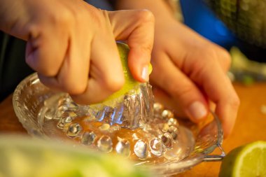 Canlı bir makro fotoğraf taze bir limonu dilimleyen ve meyve suyunu renkli bir salatanın üzerine sıkan bir kadını yakalıyor, narenciye dokusunu ve mutfak faaliyetlerindeki tazeliği vurguluyor..