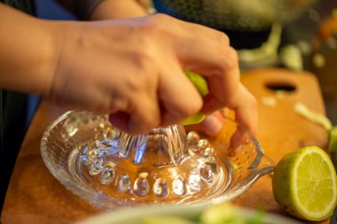 Canlı bir makro fotoğraf taze bir limonu dilimleyen ve meyve suyunu renkli bir salatanın üzerine sıkan bir kadını yakalıyor, narenciye dokusunu ve mutfak faaliyetlerindeki tazeliği vurguluyor..
