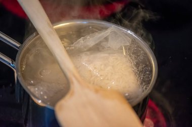 Samimi bir mutfak sahnesinde pilav hazırlayan bir kadın, tencereden kaynar su buharı gibi.