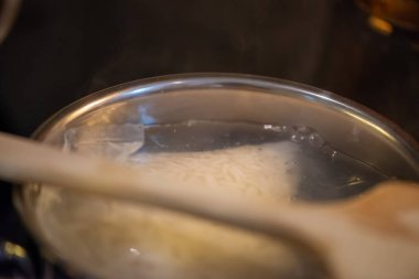 Samimi bir mutfak sahnesinde pilav hazırlayan bir kadın, tencereden kaynar su buharı gibi.