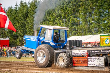 Aarhus, Danimarka. 16 Ağustos 2025 Güçlü makinelerin neşeli festival kalabalığından önce ağır topları çamura sürüklediği bir yarışma..