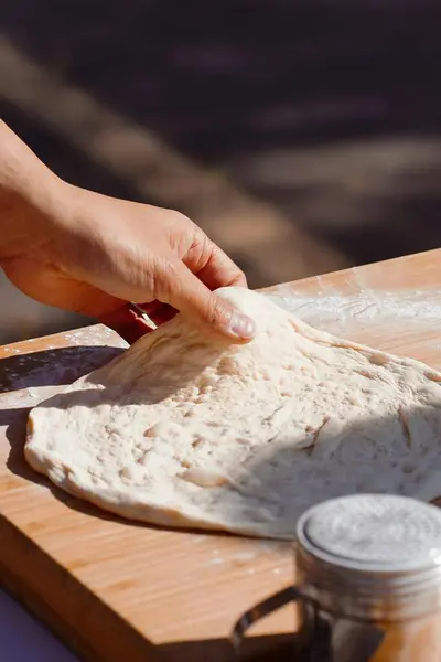 Kadın elleri masada hamurla pizza yapıyor.