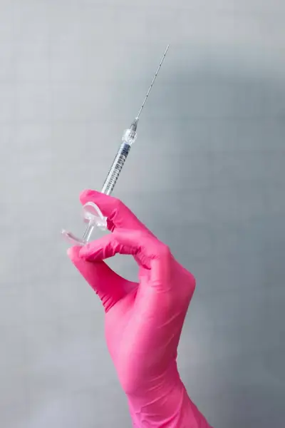 Eldivenli doktor elinde şırınga ve pembe arka planda iğne tutuyor, yakın plan.